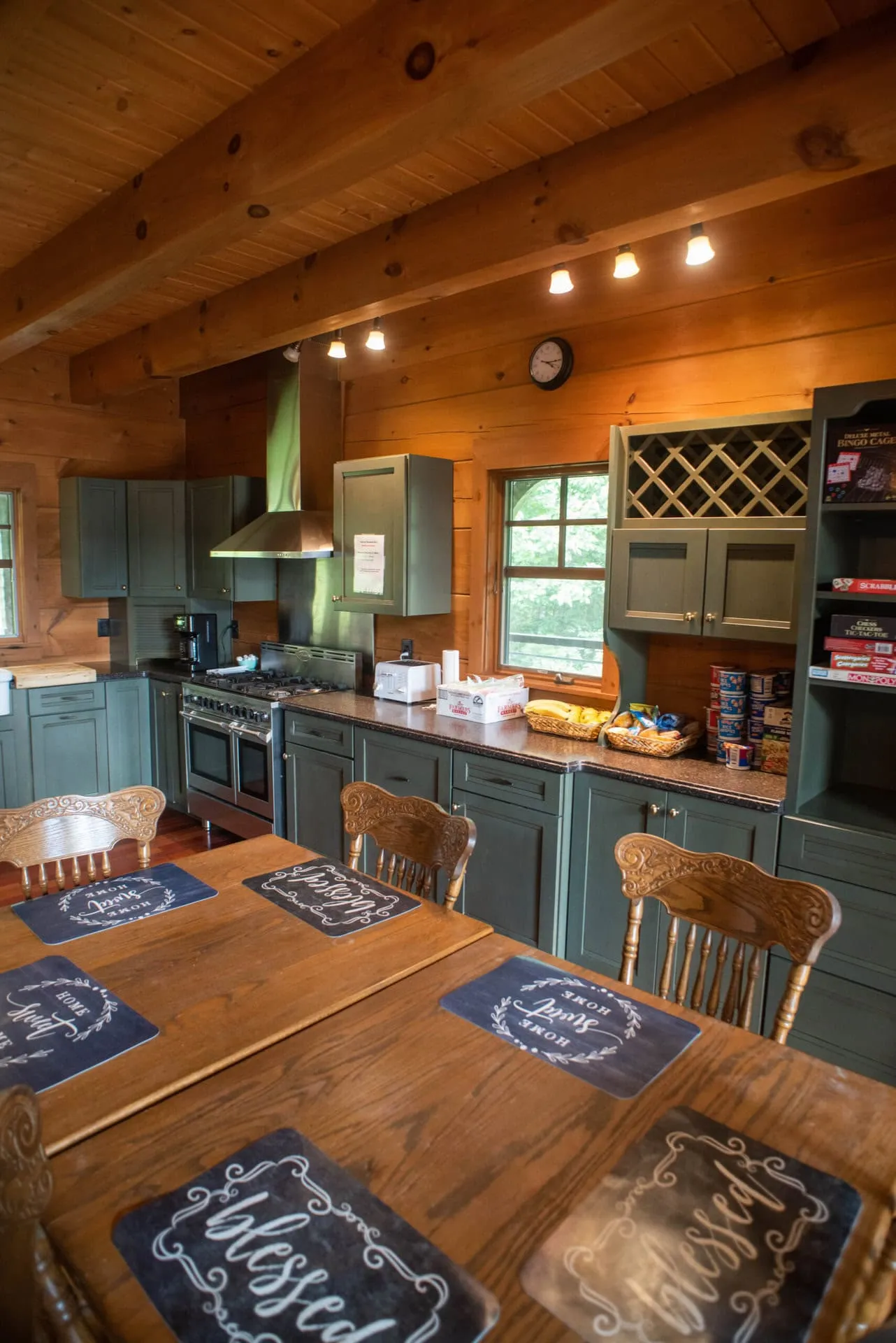 A timber-framed cabin kitchen with green cabinets and a long dining table