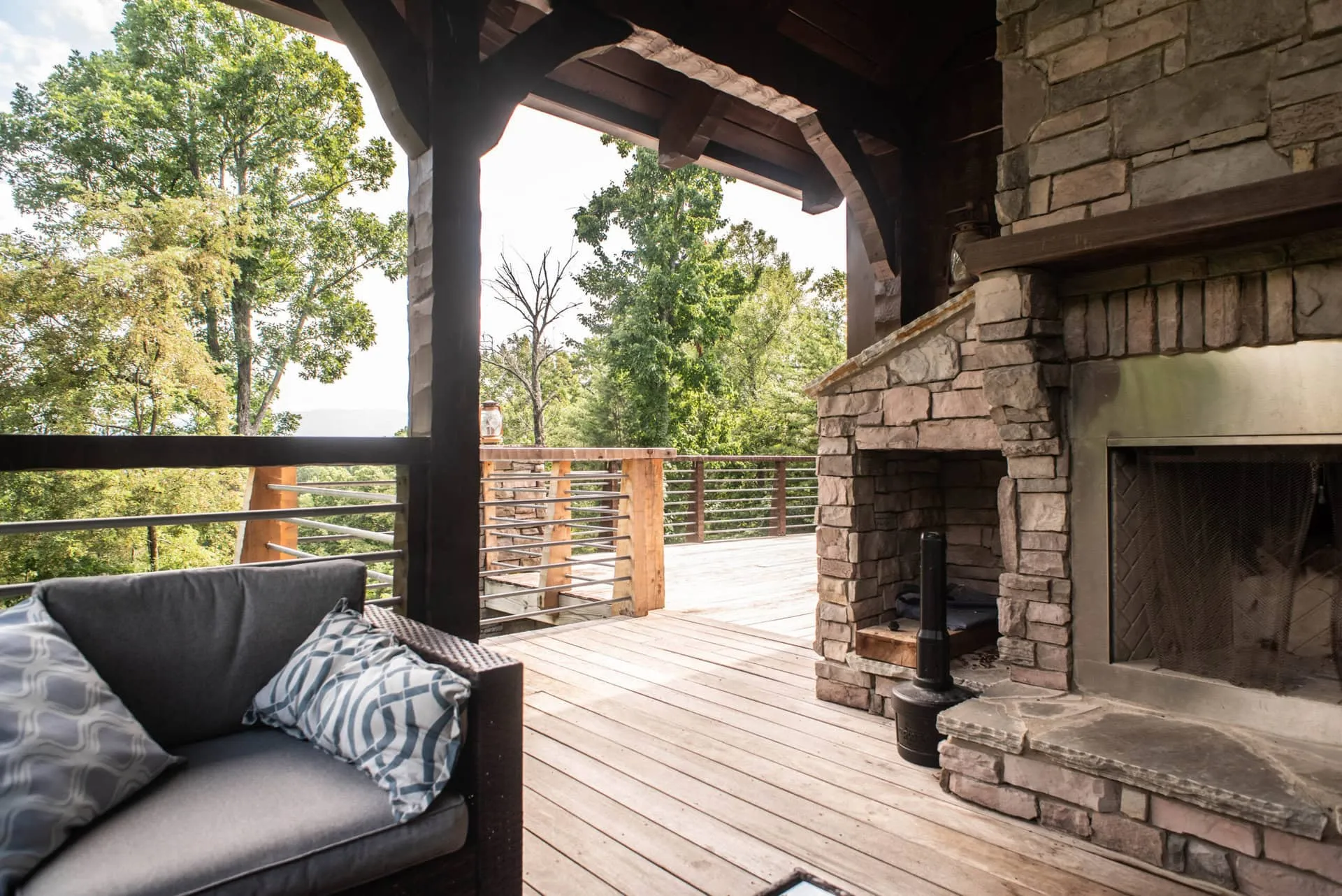 A covered cabin deck with a stone fireplace and outdoor sofa