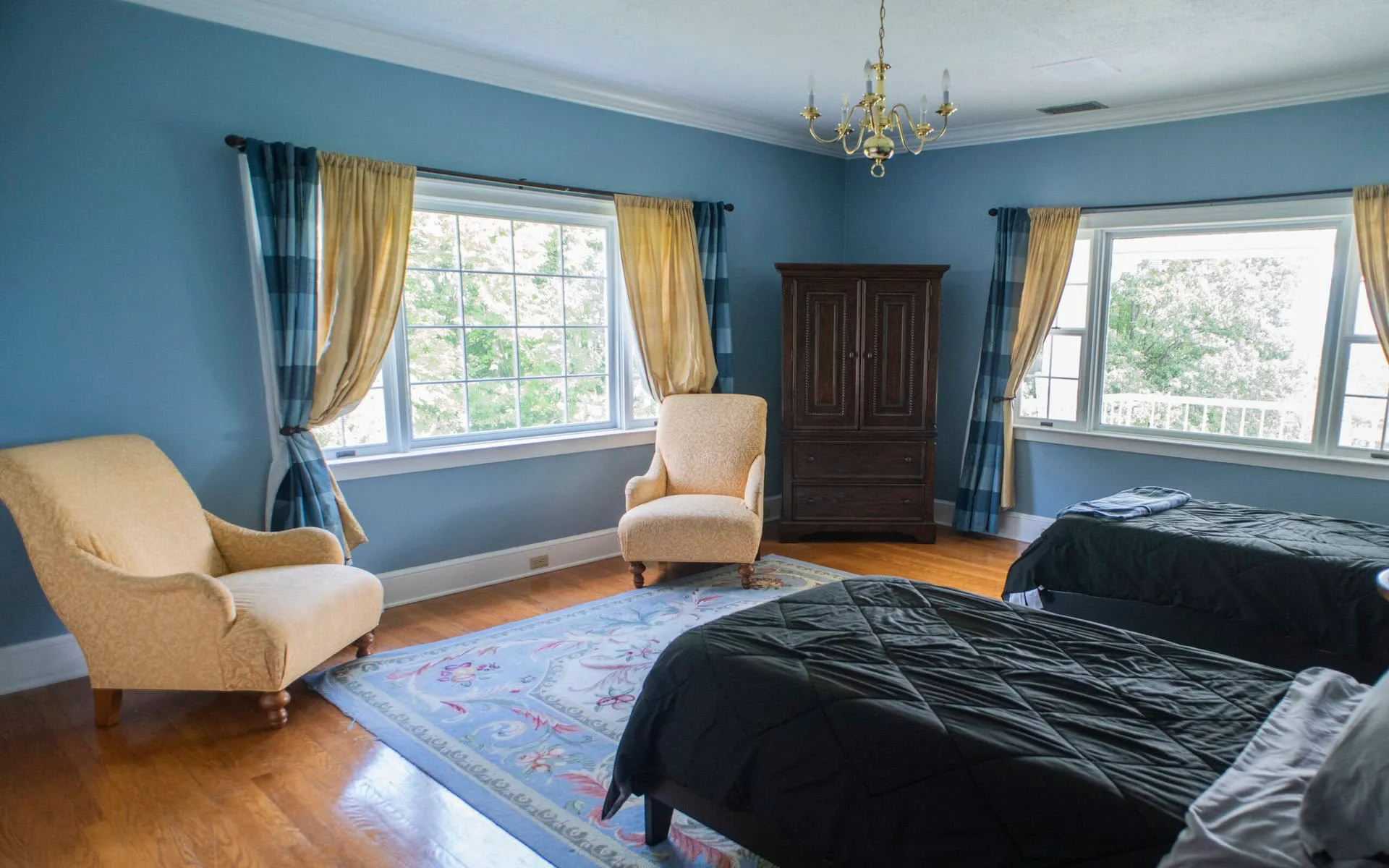 A client bedroom with two beds, armchairs and windows on two walls