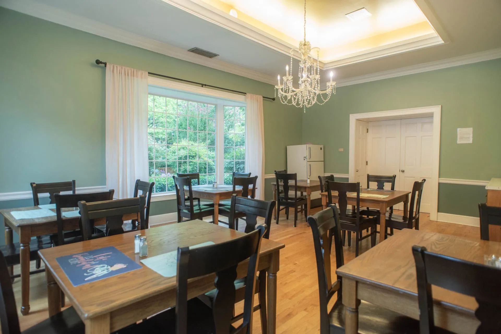 The dining room with wooden tables, a chandelier and a garden window